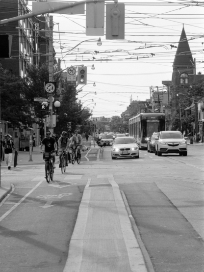 Cyclists, cars, pedestrians, and a streetcar approach across a busy intersection. 