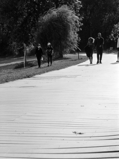 A high key photo of couples walking on and beside a boardwalk. The bright sun makes the boardwalk brilliant. 