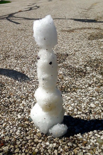 Black and white image of a little snowman. Image shows a small snowman of four segments built on the pavement, melting away in warm temperatures.