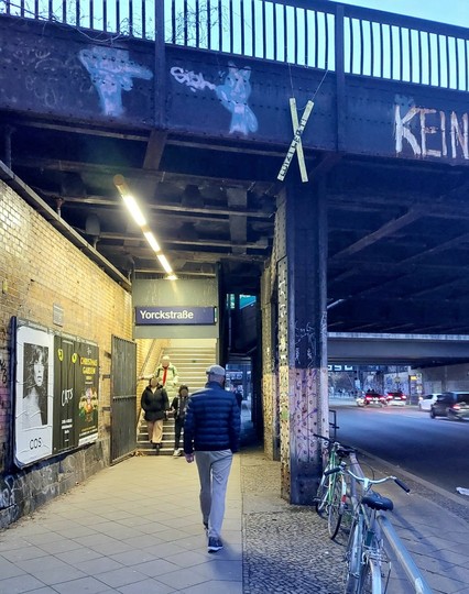 Von der stark befahrenen Straße abgesperrter Gehweg, der unter der Bahnbrücke auf den Treppenaufgang zum S-Bahnhof Yorckstraße zuführt. Ein häßlicher, lauter Ort, den man schnell durchhastet. 
Von der Bahnbrücke hängt ein schmales gelbes Warnkreuz mit der Aufschrift "Lützi lebt!".