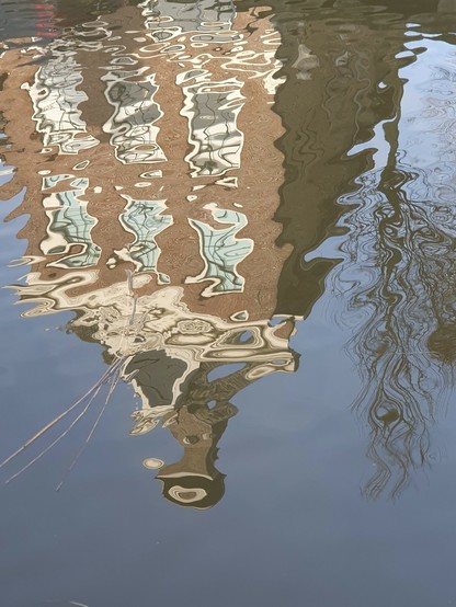 Spiegeling van een oude gevel in de Franekertrekvaart
Je ziet de gevel met een torenachtig sierornament.
Zes ramen worden gespiegeld. Blauwe lucht. Naast het huis staat een kale boom. Het is winter.