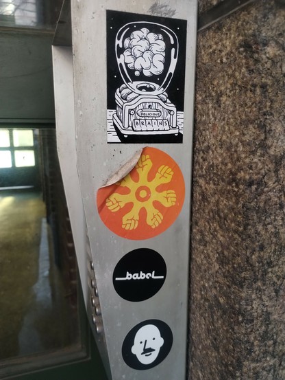 An apartment intercom on the street, shot from side, with four stickers stuck onto it.
