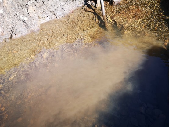 Looking down into the river Nent, the riverbed is obscured by silt billowing up from digging and levering out stones with a pinch bar. 