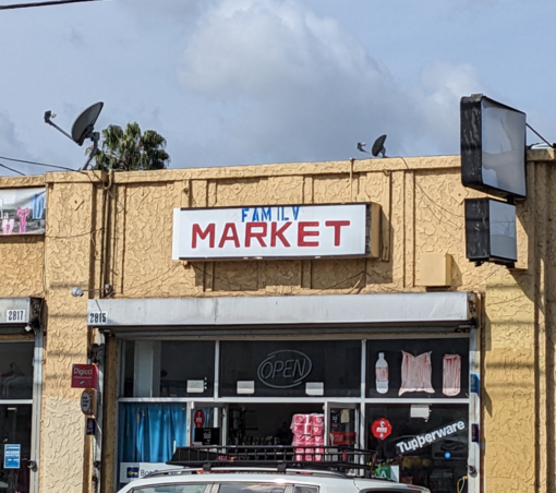 Corner store with a sign that says Family Market. there's a Tupperware sign in the window