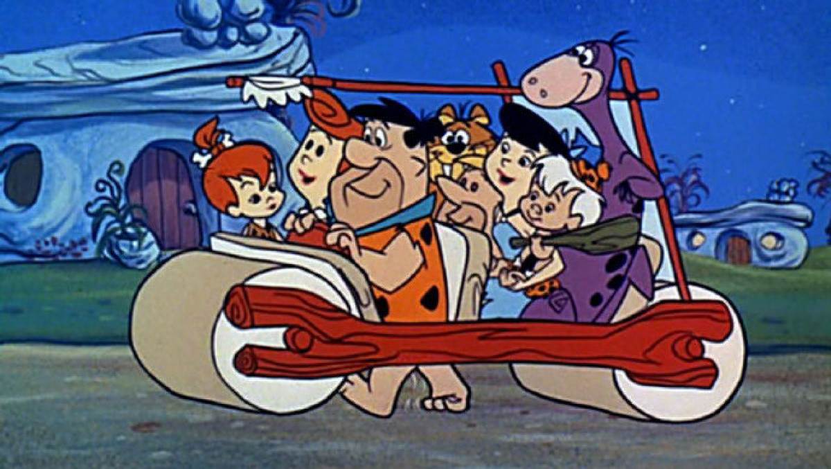 The cast of the Flintstones in Fred&#39;s car as he walks along, &quot;driving&quot; it