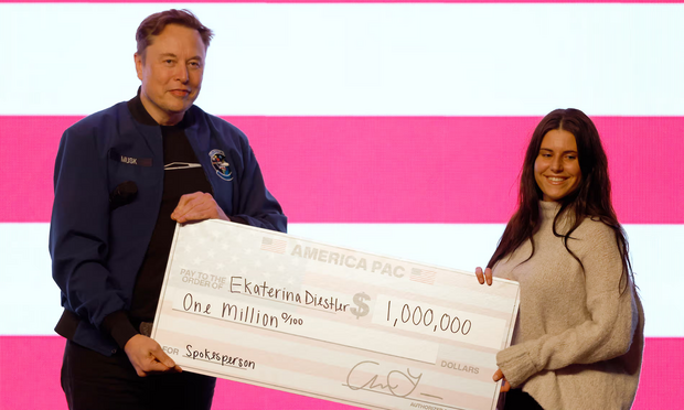 Elon Musk hands a smiling woman a giant one million dollar check.  She is being paid for being a "spokesperson," though she admitted later that she had only voted for Musk's preferred candidate in the election because she was paid to do so.