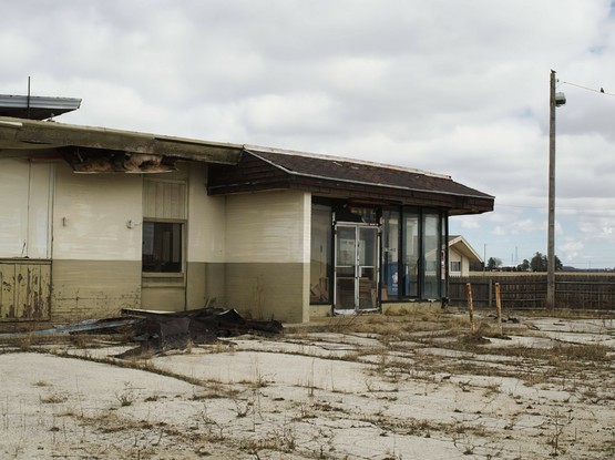 A derelict building fronted by a parking lot with weeds growing amidst the cracks.