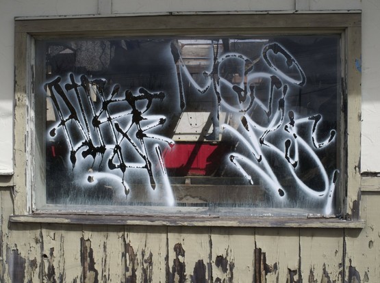 A window in a rotted wooden frame with graffiti spray painted on the glass