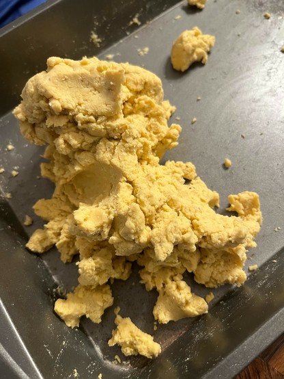 A close-up of a mound of yellow dough  on a gray baking tray. The texture appears crumbly and slightly coarse.