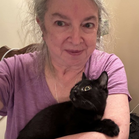 Photo: me holding the new kitten after we arrived home last night. Black kitten rests his paw on my arm, his head by my shoulder as he looks to the left. I'm wearing a purplish short sleeve shirt and look goofily happy and like I haven't combed my hair.