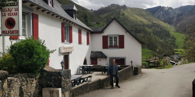 Único hotelito de Santa Grazi. Paredes blancas, ventanas rojas, tejado pirenaico. Al fondo se ven montes altos, y en frente posa el señor Pertardez.
