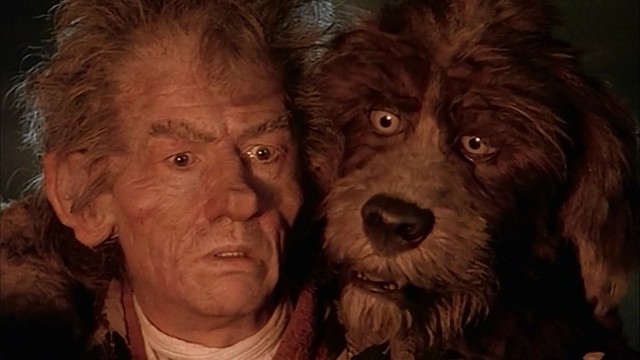 Jihn Hurt in makeup with a puppet dog in The Storyteller.