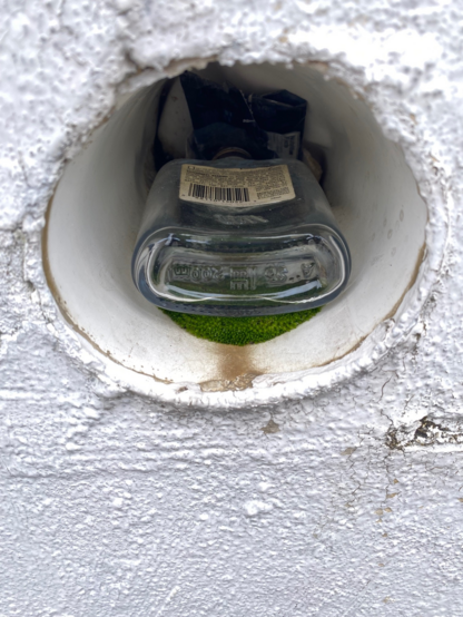 Color image of an alcohol bottle stashed in a circular drainage tile at an automobile rental facility, Akron, Summit County, Ohio, USA. 