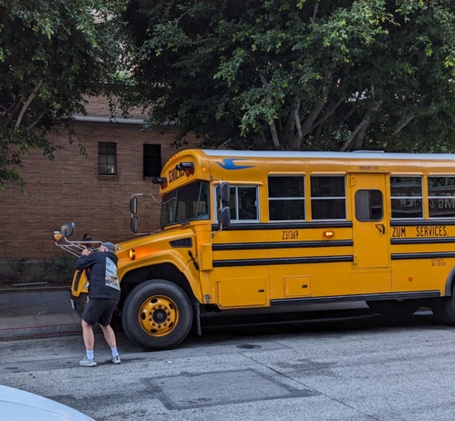 Man pointing a camera at the mirror of a parked school bus