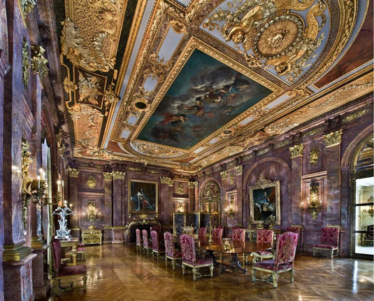 A baroque explosion of dark pink marble, gilt, fluted Corinthian columns, and parquetry on the floor. 