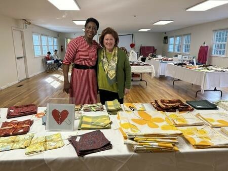 Two women standing behind a table with fabric folded into squares.