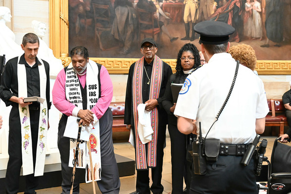 Three men in liturgical stoles and a woman in a priest collar are in the capitol rotunda. A policeman with his back to the camera looks on. 