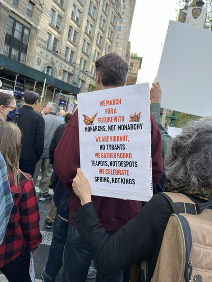 A sign that says “We march for a future with monarchs, not monarchy. We are vibrant - no tyrants. We gather round teapots, not despots. We celebrate spring, not kings.”