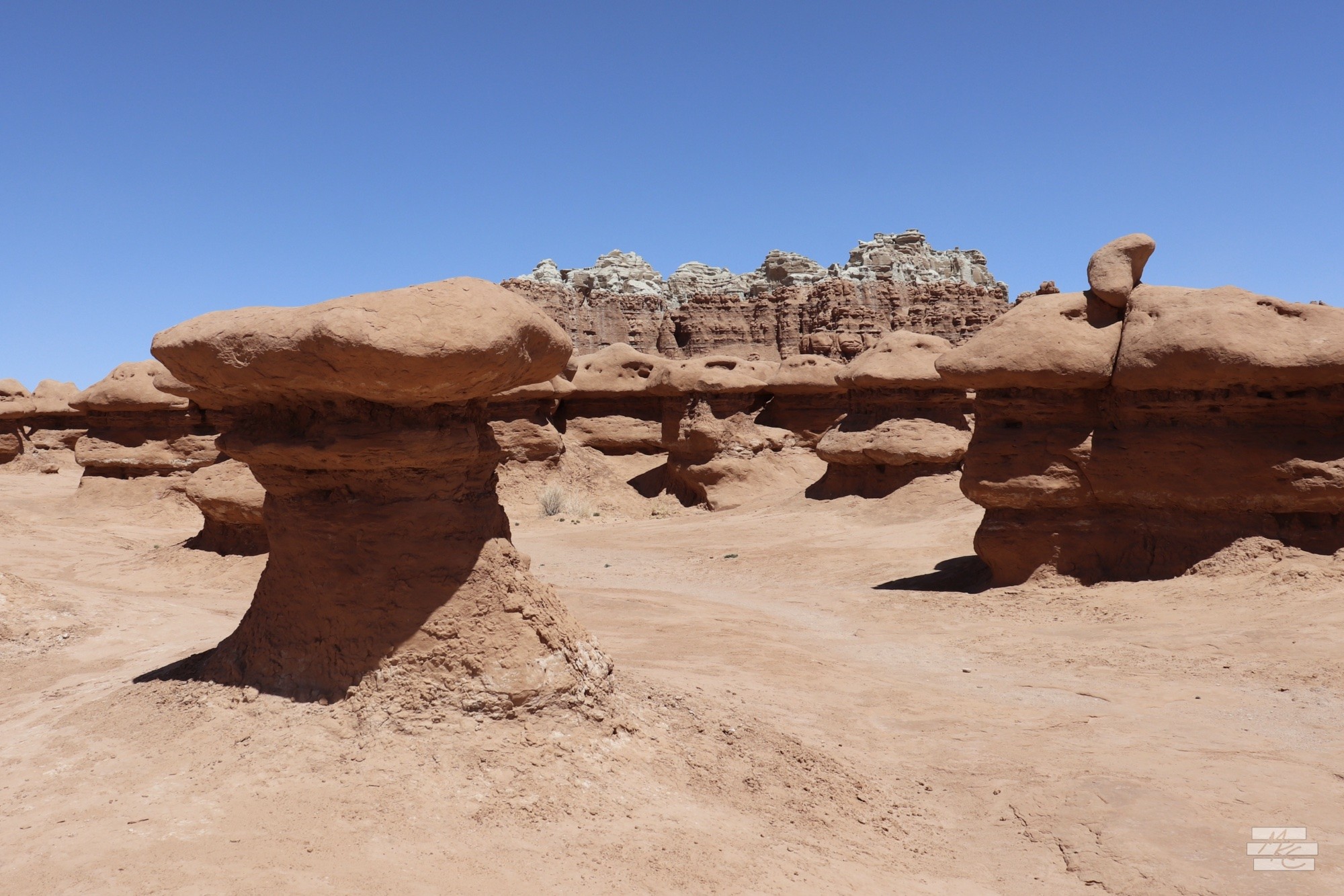 Photograph of a standalone red rock hoodoo backed by a connected row of hoodoos all with similar striations at the same level showing the layers of the rock formation and erosion. Photograph of a standalone red rock hoodoo backed by a connected row of hoodoos all with similar striations at the same level showing the layers of the rock formation and erosion.
