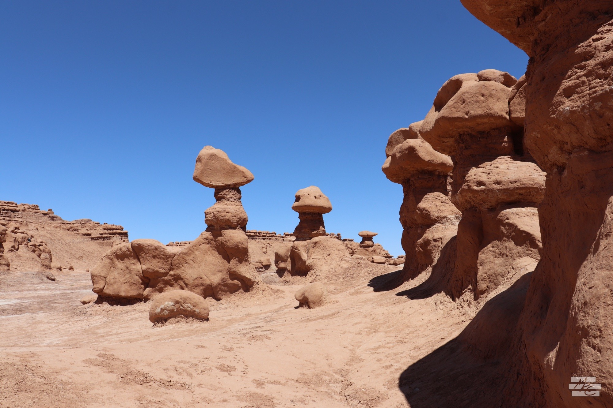 Photograph of a run of red rock hoodoos leading out to a few disconnected clusters, some casting deep shadows in the bright sunlight. Photograph of a run of red rock hoodoos leading out to a few disconnected clusters, some casting deep shadows in the bright sunlight.