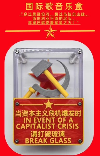 A bright red promotional poster for a novelty music box. At the top, large yellow Chinese characters read “国际歌音乐盒” (The Internationale Music Box), followed by a quote: “穿过第聂伯河，翻过乌拉尔山脉，西伯利亚平原的尽头，那里还燃烧着星星之火！” (“Crossing the Dnieper River, over the Ural Mountains, at the end of the Siberian plains, there still burns the spark of the stars!”). Below the text is a yellow star graphic. The main focus is a clear plastic box mounted on a white background. Inside the box are a 3D hammer and sickle crossed in front of a red star. Attached to the front of the box is a red and yellow plaque with both Chinese and English text: “当资本主义危机爆发时 IN EVENT OF A CAPITALIST CRISIS 请打破玻璃 BREAK GLASS.” Four screws are visible at the corners of the box, giving it the appearance of an emergency break-glass case.