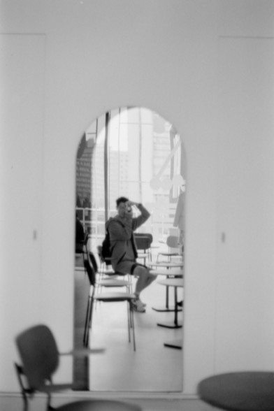 Lucky SHD 400

**English Alt Text:** A black and white photograph showing a reflection of a person sitting on a chair in front of a table, seen through an arched mirror. The person appears to be adjusting glasses or shielding eyes with a hand. The background includes several chairs and tables, and a large window with a view of buildings outside.

**Chinese Alt Text:** 一张黑白照片，通过一个拱形镜子反射出一个人坐在椅子上，面前有一张桌子。这个人似乎在调整眼镜或用手遮挡眼睛。背景中有几张椅子和桌子，还有一扇大窗户，可以看到外面的建筑物。