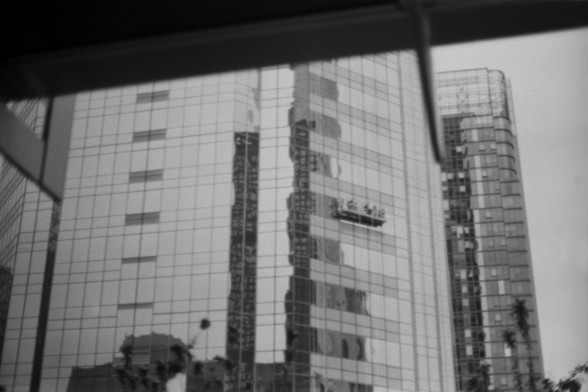 Lucky SHD 400

**English:**
A black and white photograph capturing the reflection of tall, modern skyscrapers in the glass facade of a building. The image shows a group of people on a suspended platform, possibly window cleaners, working on the exterior of one of the buildings. The scene is urban, with a focus on the architectural details and the activity taking place.

**Chinese:**
一张黑白照片，捕捉到高楼大厦在建筑玻璃幕墙上的倒影。图片中显示一群人在悬挂平台上，可能是擦窗工人，正在其中一栋建筑的外部工作。场景是城市化的，重点展示了建筑细节和正在进行的活动。