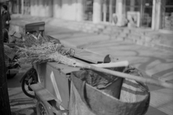 Lucky SHD 400

**English:**
A black and white photograph of a street scene featuring a cart filled with cleaning tools and supplies. The cart includes brooms, dustpans, and bags, suggesting it is used for street cleaning or maintenance. The background is slightly blurred, showing a street with buildings and columns.

**Chinese:**
一张黑白照片，展示了街道场景，其中有一辆装满清洁工具和用品的手推车。手推车上有扫帚、簸箕和袋子，表明它用于街道清洁或维护。背景稍微模糊，显示了一条有建筑和柱子的街道。