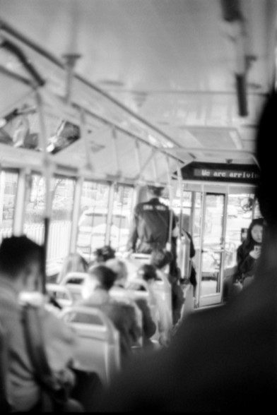 Lucky SHD 400

**English:**
A black and white photograph taken inside a public transportation vehicle, likely a bus or tram. The interior is filled with passengers, some seated and some standing. The scene is slightly blurred, capturing the motion and activity within the vehicle. A sign at the front reads "We are arriving."

**Chinese:**
一张黑白照片，拍摄于公共交通工具内部，可能是公交车或有轨电车。车内乘客众多，有些坐着，有些站着。场景稍微模糊，捕捉了车内的运动和活动。前方有一个标志写着“We are arriving (我们即将到达）”。
