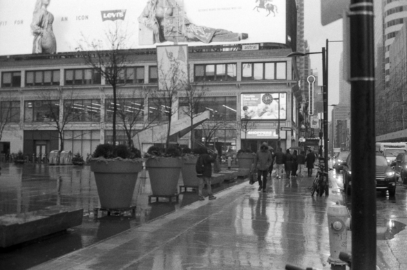 The square is empty, glistening wet as pedestrians, bundled against the cold, walk by. 