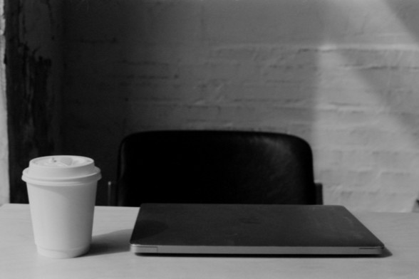 Lucky SHD 400

**English Alt Text:**
"A black and white photograph of a workspace setup. The image features a closed laptop placed on a table, with a white disposable coffee cup with a lid positioned to the left of the laptop. In the background, there is a black office chair and a white brick wall."

**Chinese Alt Text:**
"一张黑白照片，展示了一个工作区的布置。图片中有一台放在桌子上的笔记本电脑，左侧有一个带盖的白色一次性咖啡杯。背景中有一把黑色的办公椅和一面白色的砖墙。"