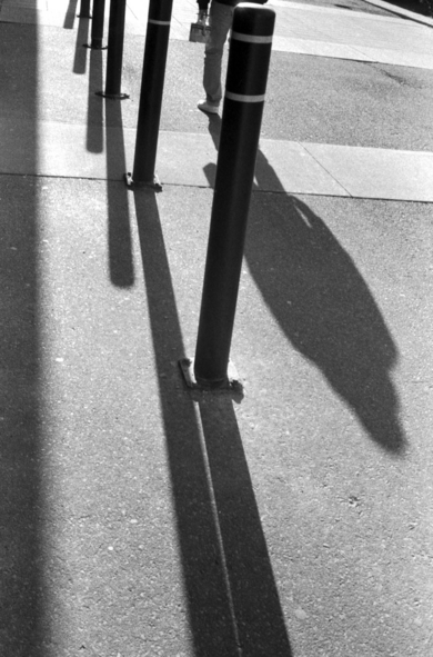 Walkway bollards cast long, deep shadow on late afternoon pavement. 