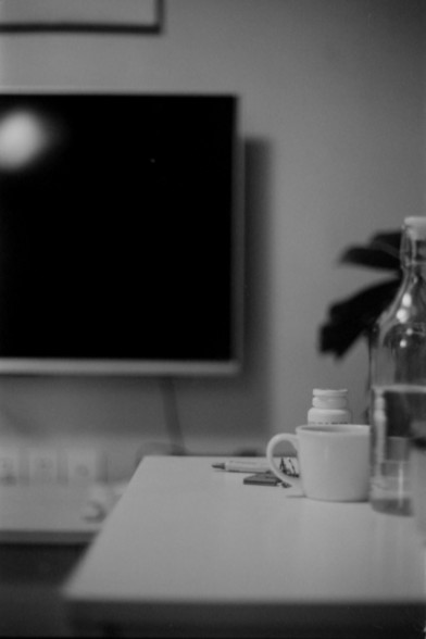 Lucky SHD 400

**English:**
A black-and-white photograph of a minimalist workspace. The image shows a desk with a coffee cup, a small stack of items, and a vase with a plant. In the background, there is a large television or monitor mounted on the wall, which is turned off.

**Chinese:**
一张极简主义风格工作空间的黑白照片。照片中有一张桌子，上面放着一个咖啡杯、一小堆物品和一个带植物的花瓶。背景中有一台挂在墙上的大电视或显示器，处于关闭状态。