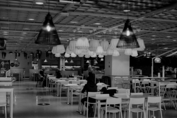 Lucky SHD 400

**English:**
A black-and-white photograph of a spacious cafeteria or dining area. The room is filled with tables and chairs, and there are large, decorative hanging lamps. A few people are seated at the tables, and the overall atmosphere is calm and relaxed.

**Chinese:**
一张宽敞的自助餐厅或餐饮区的黑白照片。房间内摆满了桌椅，并悬挂着大型装饰灯。几个人坐在桌旁，整体氛围宁静而轻松。