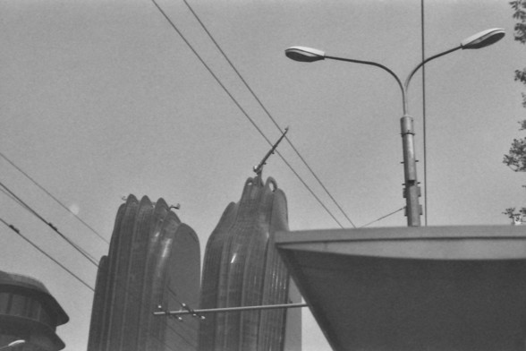 **English Alt Text:**
The image depicts an urban scene with a focus on overhead electrical wires and a streetlight. The wires are connected to two cylindrical structures, possibly insulators, which are mounted on a horizontal bar. The streetlight has a modern design with two lamps extending from a single pole. The background includes part of a building and a clear sky, suggesting it is daytime.

**Chinese Alt Text:**
这张图片展示了一个城市场景，主要聚焦于头顶的电线和一盏街灯。电线连接着两个圆柱形结构，可能是绝缘子，它们安装在一根水平杆上。街灯设计现代，单根灯杆上延伸出两…