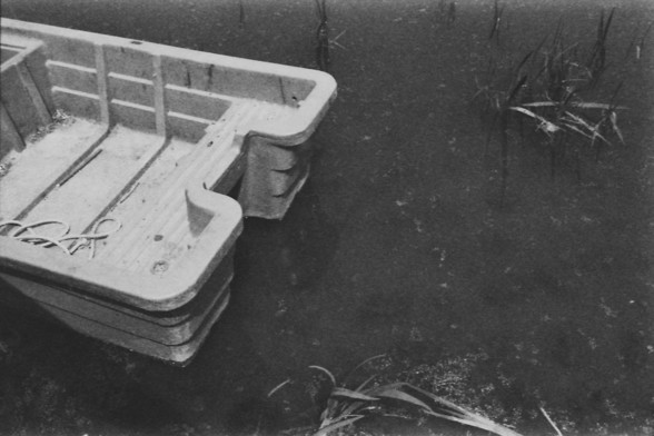 **English:**
A black-and-white photograph of a small boat floating on a body of water. The boat appears to be empty and is partially submerged. There are some plants visible in the water near the boat.

**Chinese:**
一个黑白照片，展示一艘小船漂浮在水面上。船看起来是空的，并且部分沉没。船附近的水中有一些植物可见。
