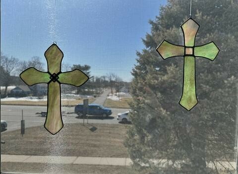 Two stained glass crosses in a window that looks out over a street with vehicles and some snow.