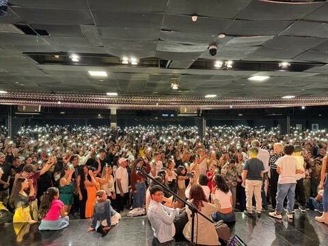 A large group of people in an indoor area holding up their phones with the flashlight on.