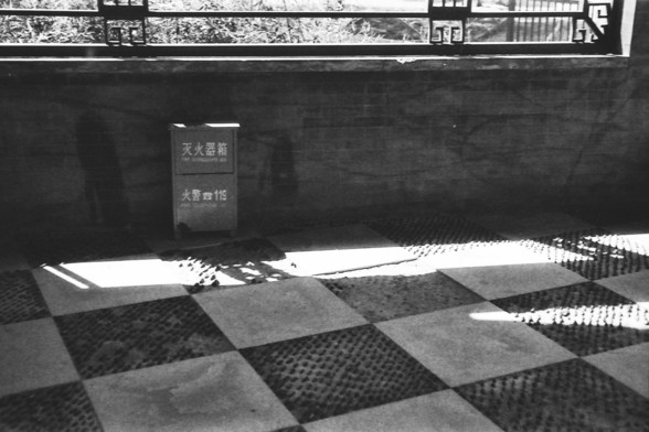 Ilford FP4 @ ISO 80

**English:**
This black-and-white image shows a scene with a large chessboard-like floor. The setting has a traditional feel, with a stone wall and a window that has wooden bars. There is a tool box of fire extinguisher by the wall with some text on it. The lighting creates a contrast, highlighting the style and giving a dramatic effect to the scene.

**Chinese:**
这张黑白图片展示了一个场景，地板上有类似棋盘的风格。场景带有传统风格，有一面石墙和一个带木质栏杆的窗户。墙边有一个灭火工具箱，上面有一些文字。光影制造出对比，突出了地面的明暗，并给场景带来了戏剧性效果。