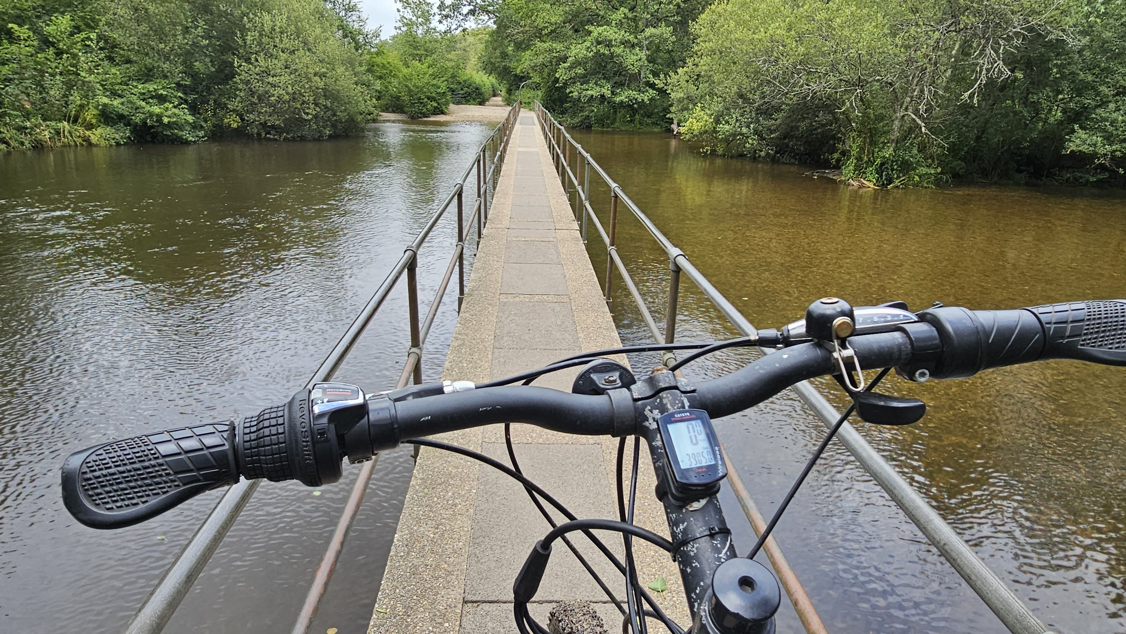 View over bike handelbars along a narrow, concrete bridge over water.