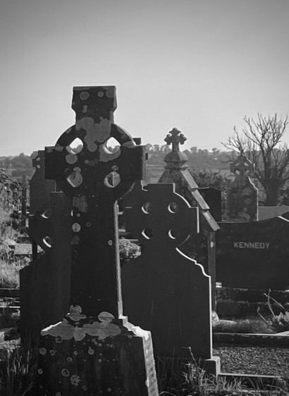 Celtic crosses encrusted with lichens jammed together in a graveyard. Backlit light shines through some of the crosses.