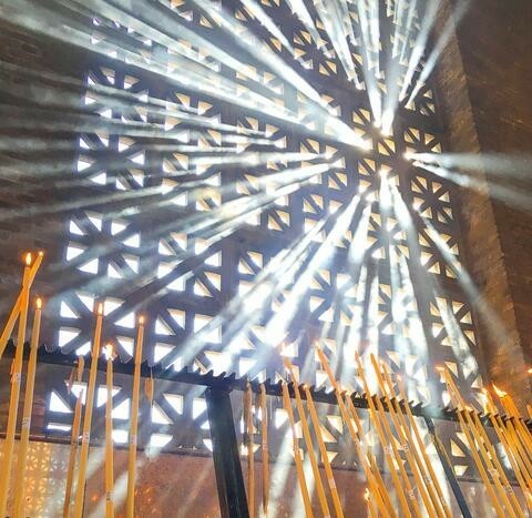 Bright light shining through a church window covered by stone tracery. Candles in the foreground.