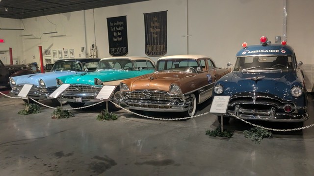 Four vintage automobiles circa 1950's. One is a blue ambulance the others are powder blue, turquoise and copper colored .