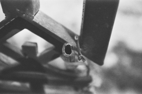 Ilford FP4 @ ISO 64

**English alt text:**  
A close-up black and white photograph of a hollow cylindrical metal piece, possibly broken or cut at the end. A small twig or fragment of debris is attached to it. The blurred background enhances the industrial and mechanical tone of the image.

**Chinese alt text (中文替代文本):**  
一张黑白特写照片，展示了一个中空的金属圆柱体，可能是被切割或损坏的。其表面附着着一根小树枝或碎片。模糊的背景增强了图像的工业与机械感。