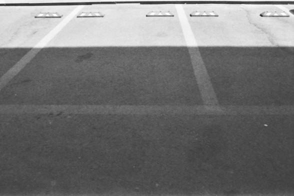 Ilford FP4 @ ISO 64

**English alt text:** A black and white image of an empty parking lot with visible parking spaces and wheel stops. The parking lot has a shadow cast across it, dividing the image horizontally.

**Chinese alt text:** 一张黑白照片，显示一个空的停车场，有明显的停车位和轮挡。停车场有阴影横向穿过，分割了图像。