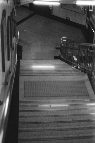 Ilford FP4 E.I. 64

**English Alt Text:**
"A black and white photograph of a staircase in what appears to be a subway or underground station. The stairs are equipped with a central handrail and are flanked by walls on either side. The lighting is artificial, casting shadows and highlighting the steps. The stairs lead upwards, suggesting an exit or an upper level."

**Chinese Alt Text:**
"一张黑白照片，展示了一个看起来像是地铁或地下站的楼梯。楼梯中央设有扶手，两侧有墙壁。灯光是人工的，投下阴影并突出了台阶。楼梯向上延伸，暗示出口或上一层。"