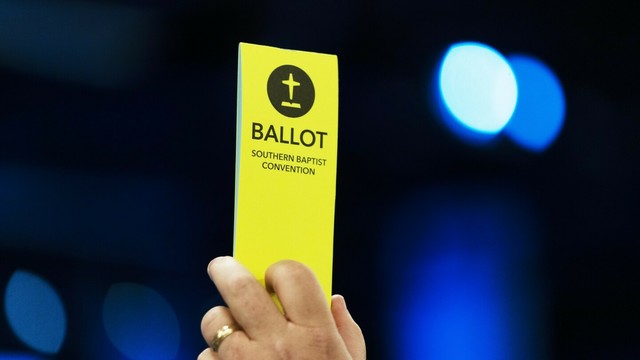A hand holding a yellow ballot that reads Ballot Southern Baptist Convention.