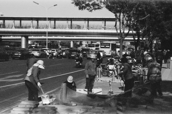 Ilford FP4 E.I. 64

English alt text: A busy urban street where construction workers are engaged in roadwork. They are wearing helmets and safety gear while handling tools and materials like bricks and shovels. Vehicles, including cars, motorcycles, and buses, are visible on the road, with an elevated pedestrian walkway and trees in the background.

Chinese alt text: 繁忙的城市街道上，建筑工人正在进行道路施工。他们戴着头盔和安全装备，使用工具和材料，如砖块和铲子。道路上有汽车、摩托车和公交车，背景中可以看到高架人行道和街道两旁的树木。