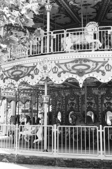**English:**
This black and white image depicts a section of a vintage carousel. The carousel is adorned with elaborate decorations, including ornate carvings and mirrors. Horses and other animals are visible, each intricately designed and painted. The structure of the carousel includes a railing and a central pole, adding to the classic aesthetic of this amusement ride.

**Chinese:**
这张黑白图片展示了一个复古旋转木马的一部分。旋转木马装饰有精美的雕刻和镜子。可以看到马和其他动物，每个都设计精美并绘有图案。旋转木马的结构包括栏杆和中央柱，增添了这种娱乐设施的经典美感。