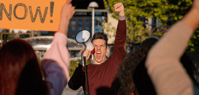 A man shouting with a megaphone, his fist raised in the air in front of a crowd.